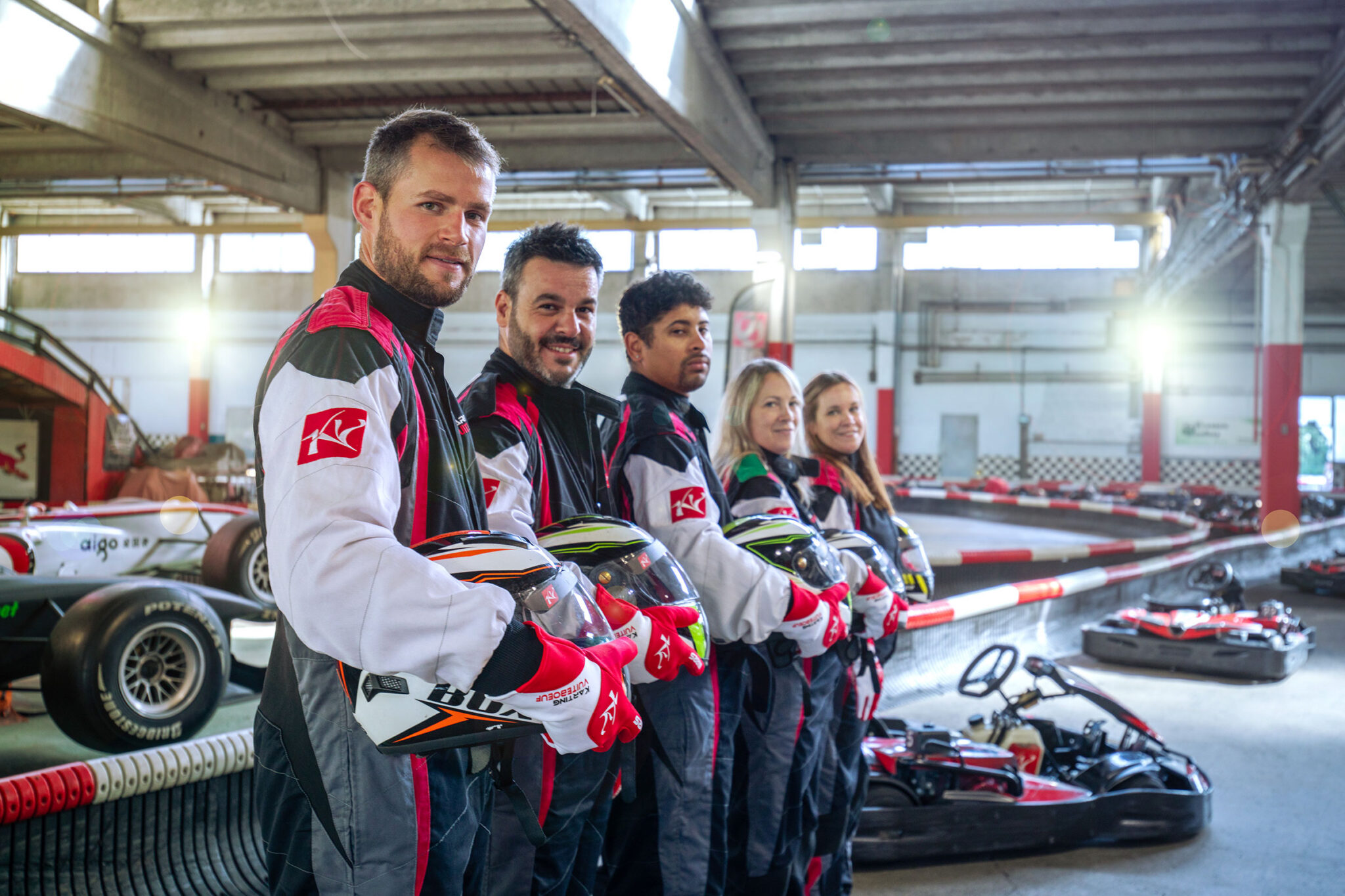 Groupe de 5 pilotes souriants en combinaison alignés avec casque à la main, Karting de Vuiteboeuf